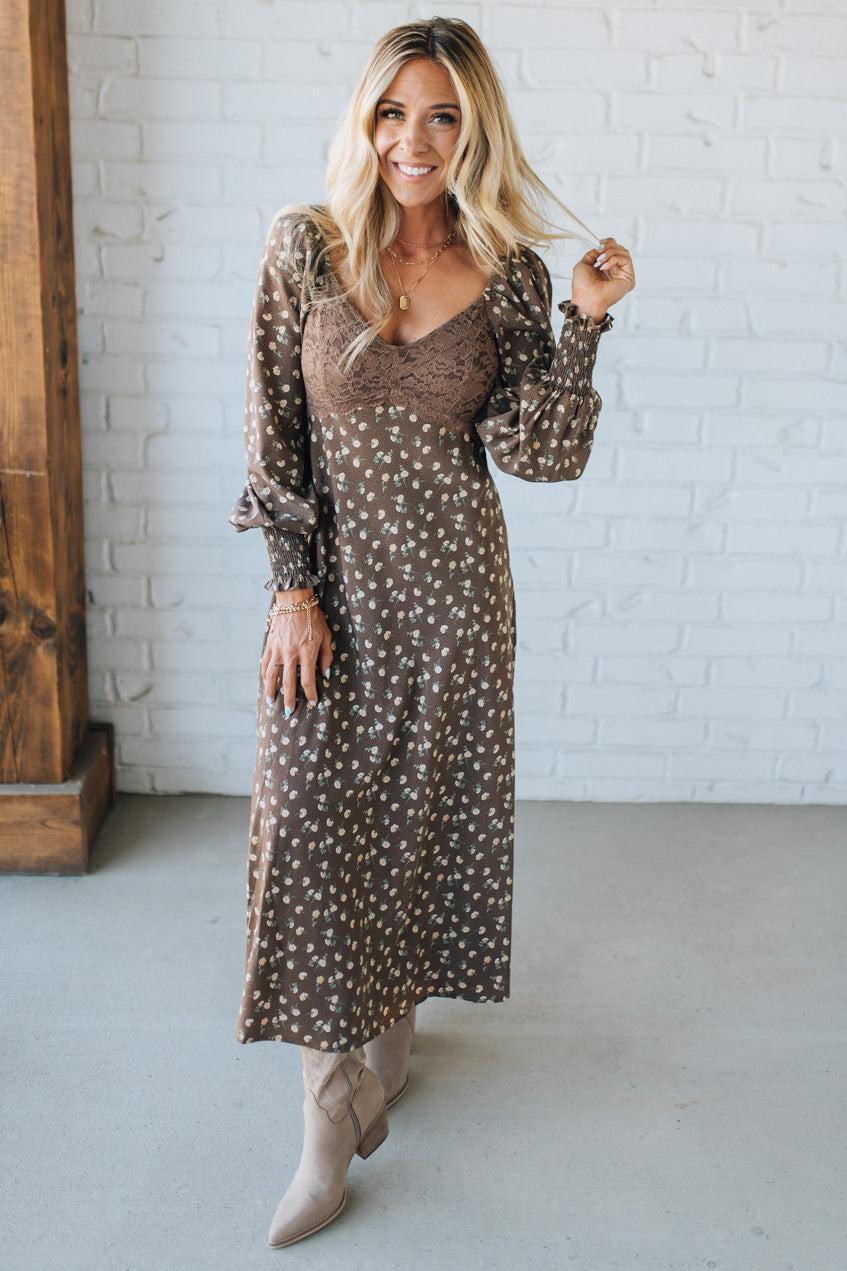Woman wearing a patterned dress standing against a white brick wall.