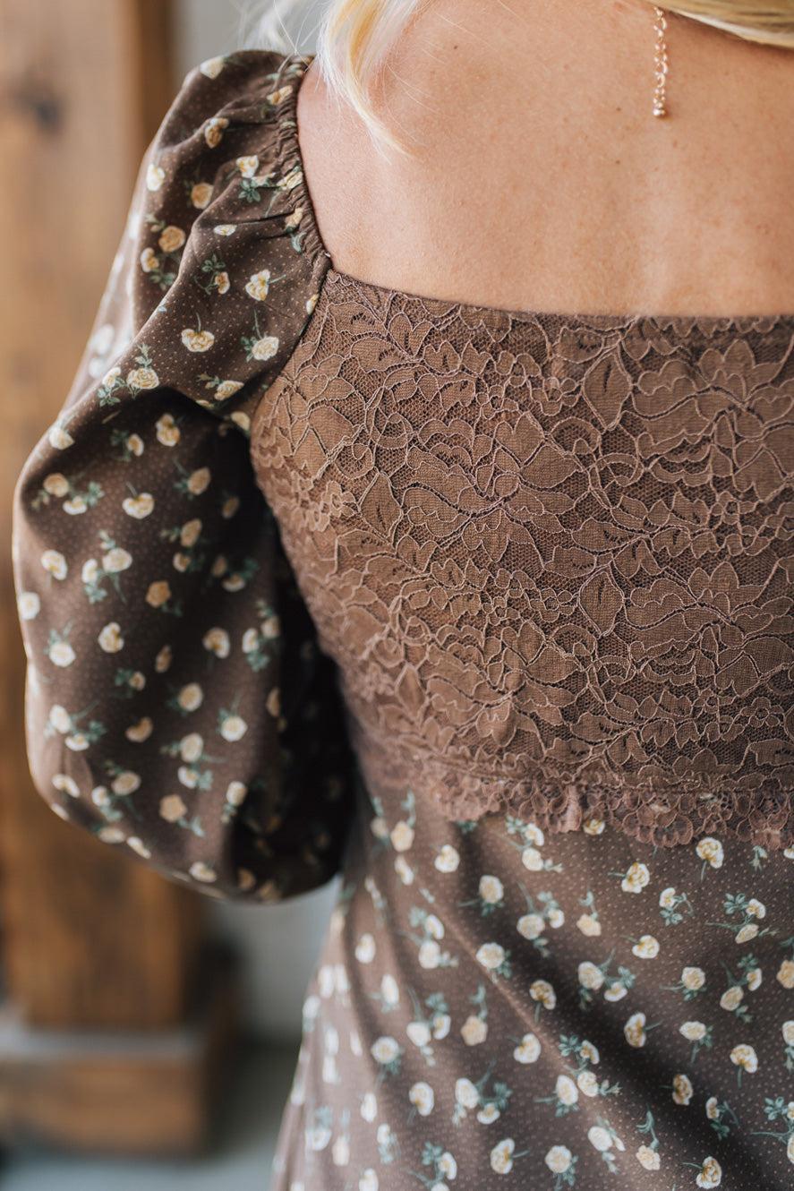 Close-up of a brown lace dress with floral sleeves against a blurred background