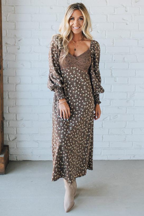 Woman wearing a brown polka dot dress against a white brick wall.