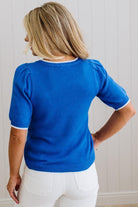 Person wearing a blue sweater with white trim against a light wooden panel background