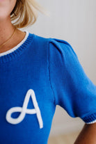 Blue sweater with a white letter 'A' on a neutral background