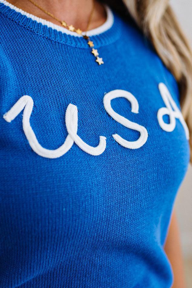 Blue sweater with white text worn by a person, close-up view.