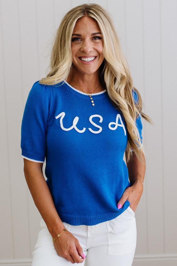 Woman wearing a blue sweater with 'USA' text against a neutral background