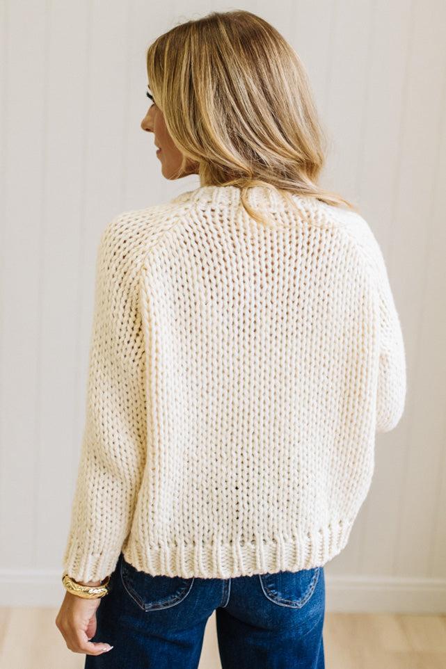 Blonde Woman in a Bright Studio wearing a cream Front Button Closure chunky sweater with red Bow Trim, Long Sleeves.