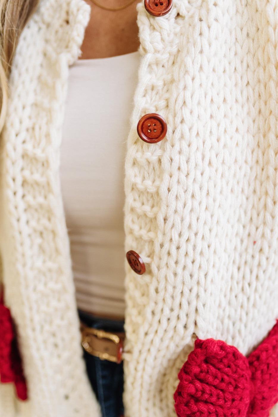 Blonde Woman in a Bright Studio wearing a cream Front Button Closure chunky sweater with red Bow Trim, Long Sleeves.