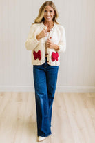 Blonde Woman in a Bright Studio wearing a cream Front Button Closure chunky sweater with red Bow Trim, Long Sleeves.
