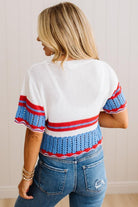 A woman shown from the back wearing a white knit top with blue and red striped details on the sleeves and hem, paired with blue jeans, set against a light beige paneled wall.
