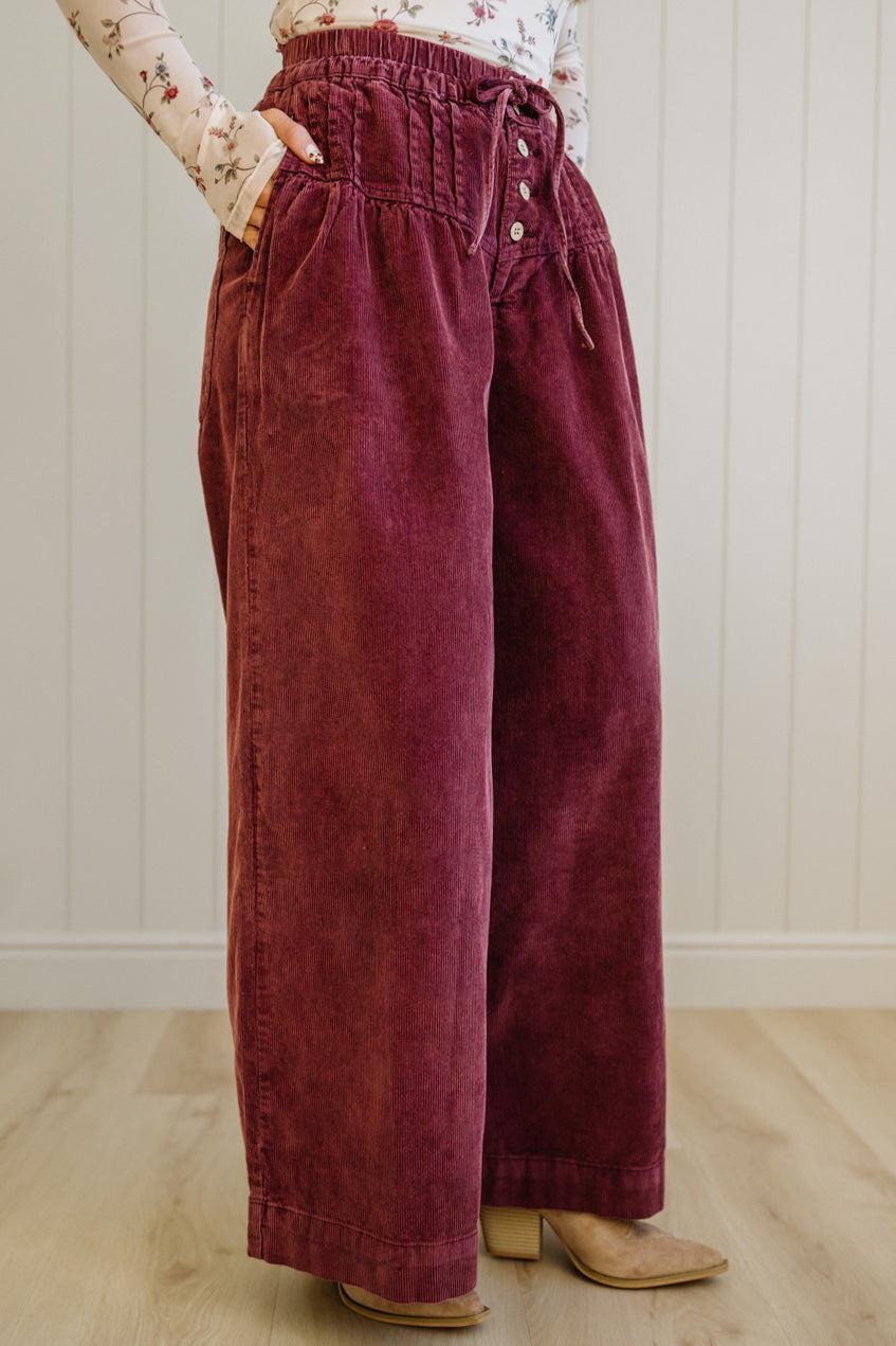 Maroon velvet pants worn by a person on a light wooden floor.