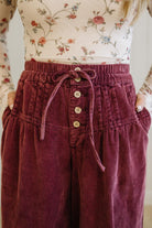 Maroon corduroy pants with a floral top worn by a person.