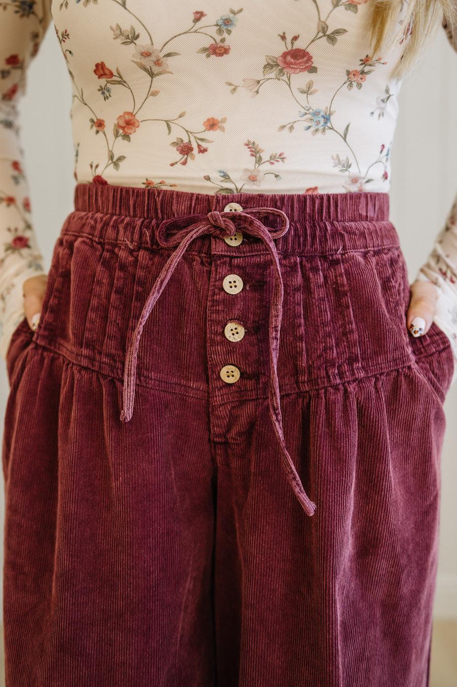Maroon corduroy pants with a floral top worn by a person.