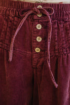 Close-up of maroon corduroy pants with button details and a drawstring.