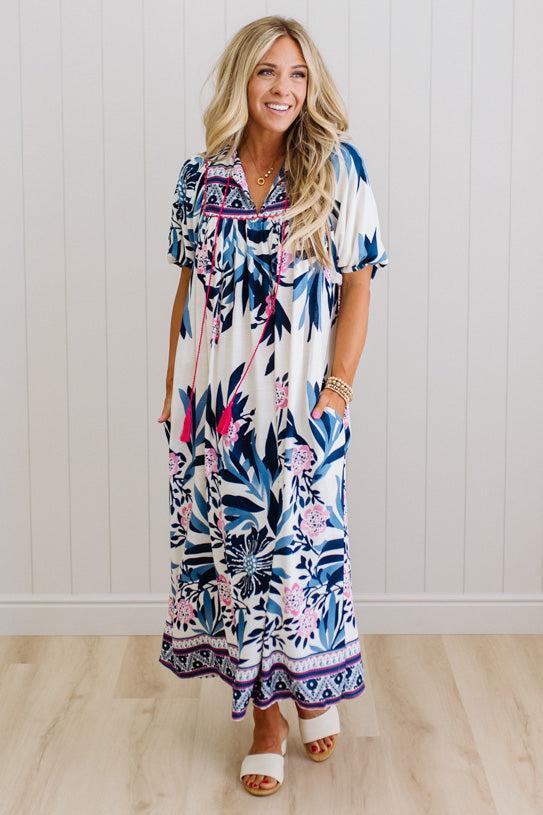 Blonde woman wearing a long printed maxi dress in blue and white with hot pink accents.
