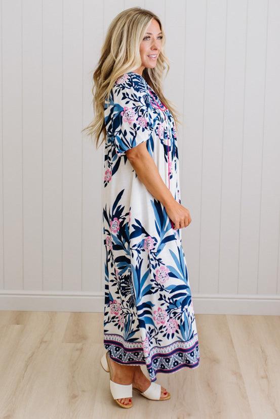 Blonde woman wearing a long printed maxi dress in blue and white with hot pink accents.