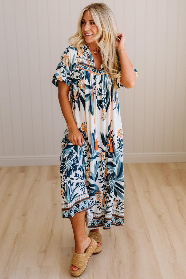 Woman wearing a tropical patterned dress standing on a wooden floor.