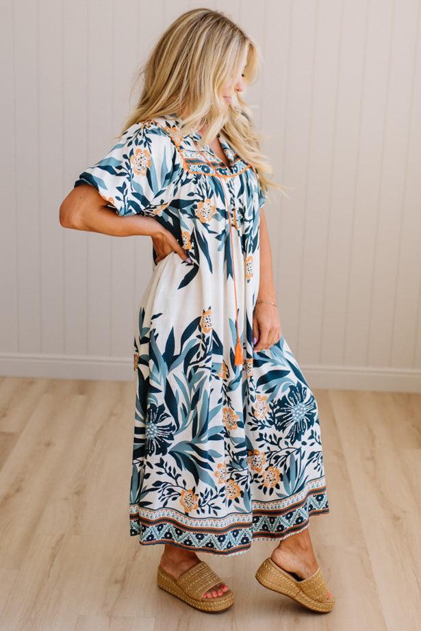 Woman wearing a floral dress standing on a wooden floor with a white wall background