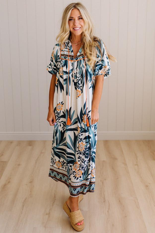 Woman wearing a floral dress standing on a wooden floor with a neutral wall background