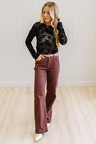 Blonde Woman Wearing A Floral Embroidered Stretch Lace Long Sleeve Top with Dark Jeans and Light Brown Belt.