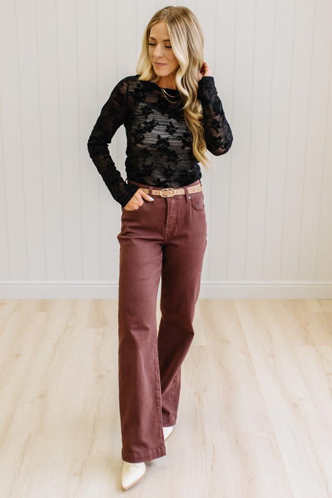 Blonde Woman Wearing A Floral Embroidered Stretch Lace Long Sleeve Top with Dark Jeans and Light Brown Belt.