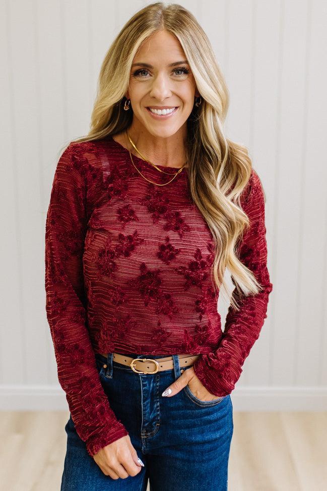Blonde Woman Wearing A Floral Embroidered Stretch Lace Long Sleeve Top with Dark Jeans and Light Brown Belt.