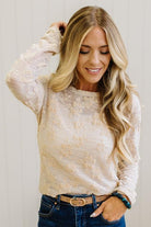 Blonde Woman Wearing A Floral Embroidered Stretch Lace Long Sleeve Top with Dark Jeans and Light Brown Belt.