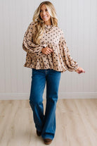 BLONDE WOMAN WEARING A WHIMSICAL POLKADOT RUFFLE PUFF BLOUSE IN LATTE STANDING AGAINST A PANELED WALL IN A BRIGHTLY LIT STUDIO.