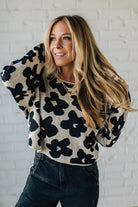 Woman wearing a black and white floral sweater against a white brick wall.