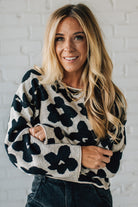 Woman wearing a black and white floral sweater against a white brick wall.