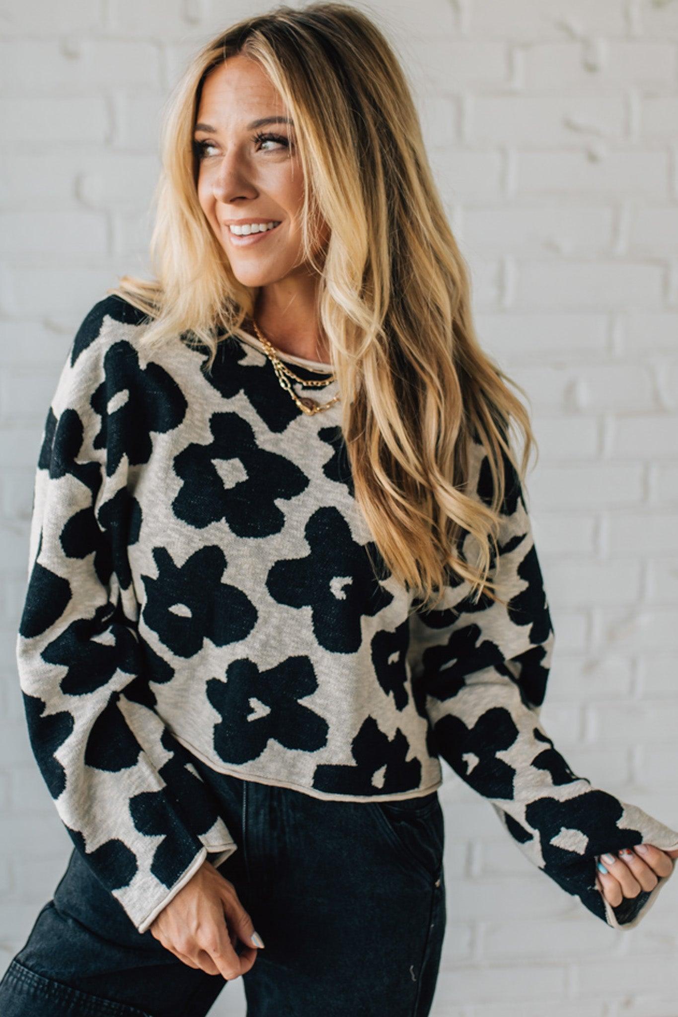 Woman wearing a black and white floral sweater against a white brick wall.