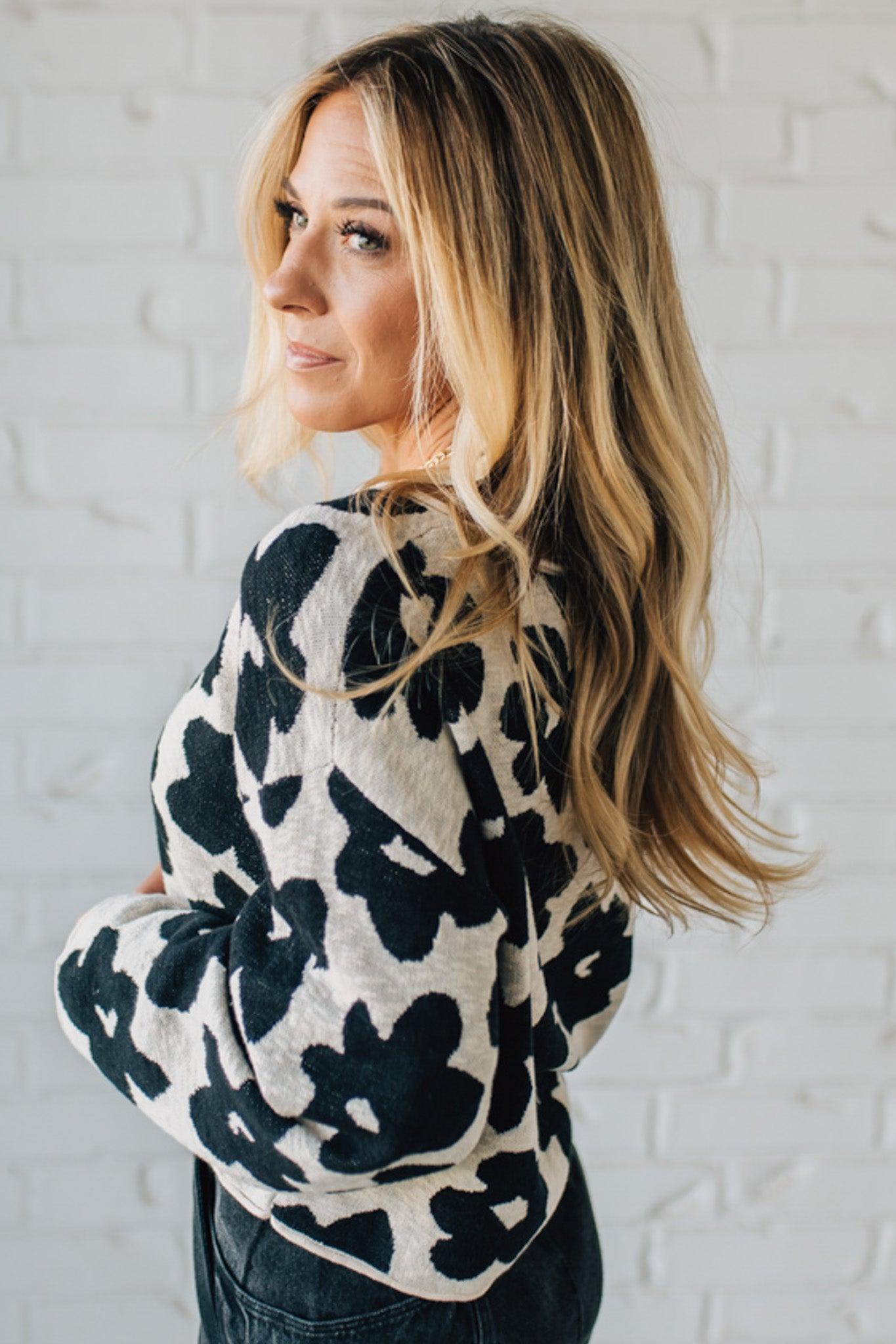 Woman wearing a black and white patterned sweater against a white brick wall.