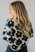Woman wearing a black and white floral patterned sweater against a white brick wall.