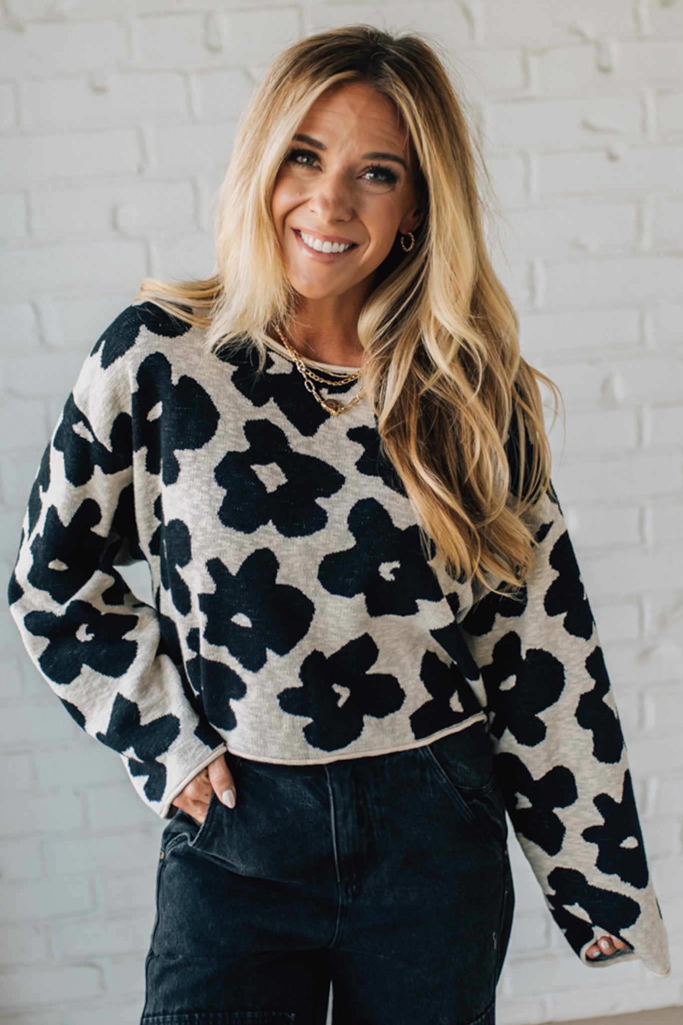 Woman wearing a black and white floral sweater against a white brick wall.