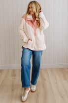 Woman wearing a white fleece jacket with pink interior, blue jeans, and white sneakers in a room with wooden flooring and a light-colored wall.
