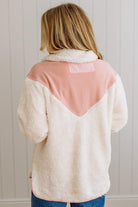 Person wearing a cream and pink sherpa jacket against a white paneled wall.