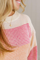 Close-up of a person wearing a pink and beige patterned sweater with a blurred background.