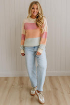 Woman wearing a colorful striped sweater and light blue jeans standing against a neutral wall.