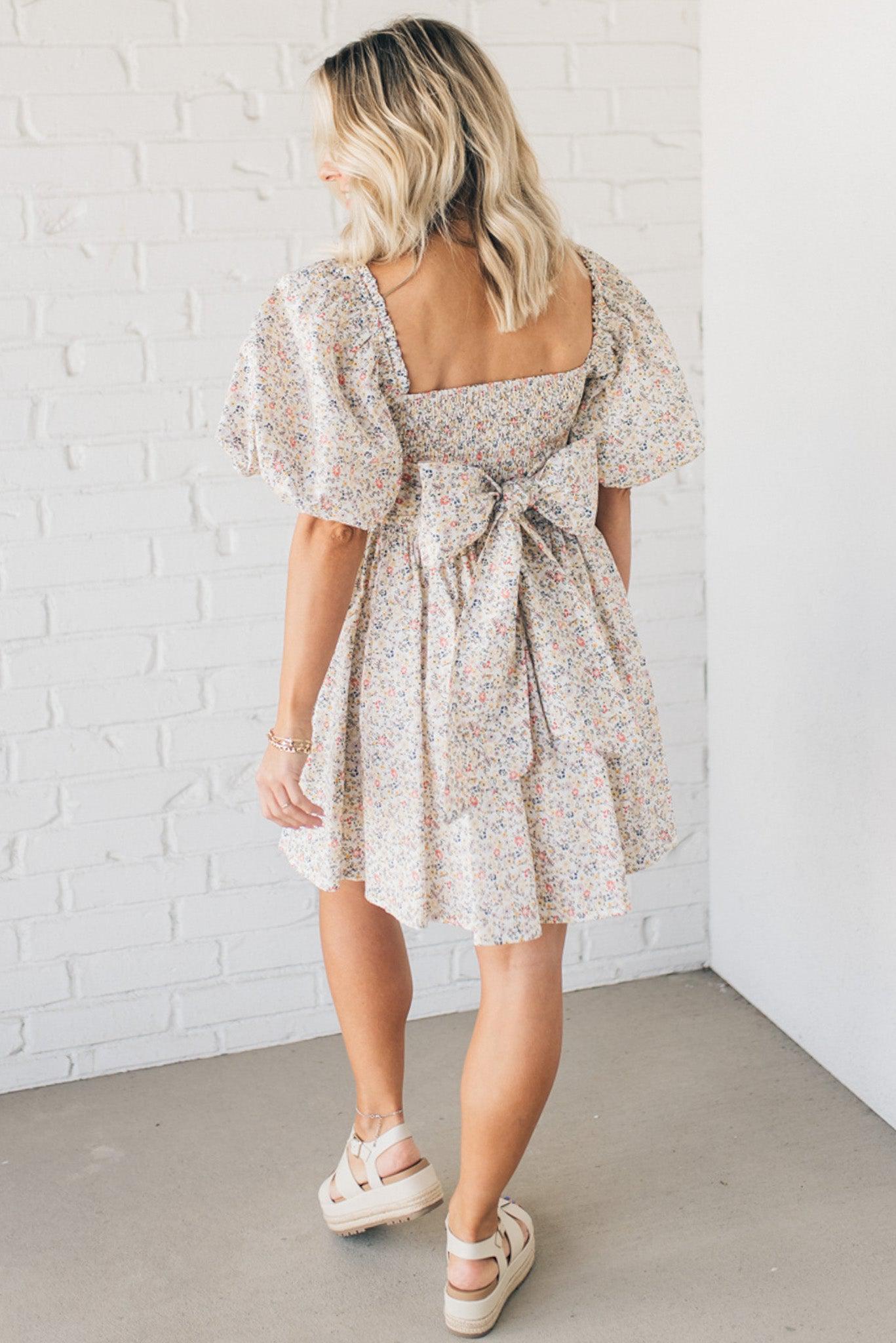Blonde woman wearing a floral dress with puff sleeves and a large statement bow at the back.