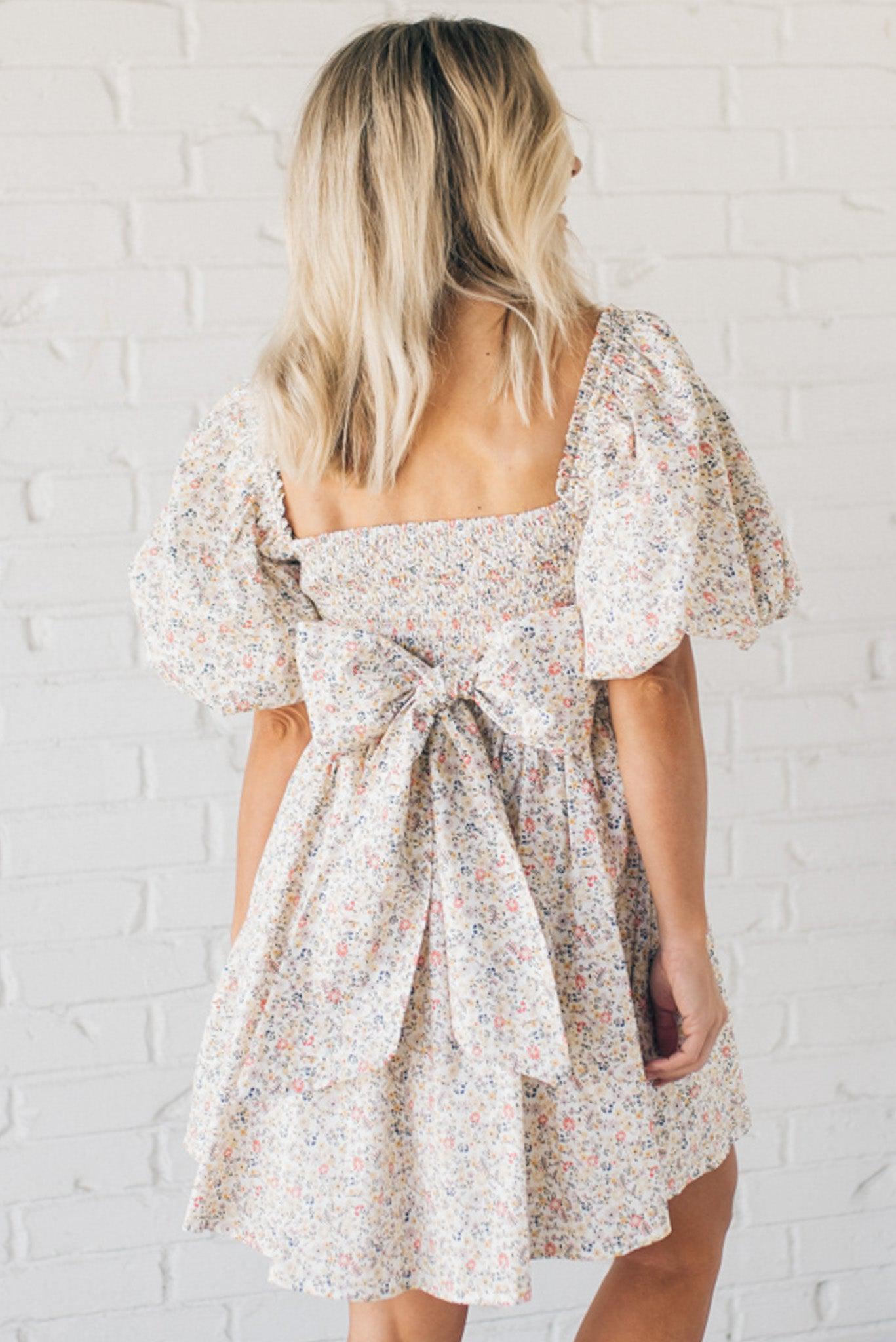 Blonde woman wearing a floral dress with puff sleeves and a large statement bow at the back.