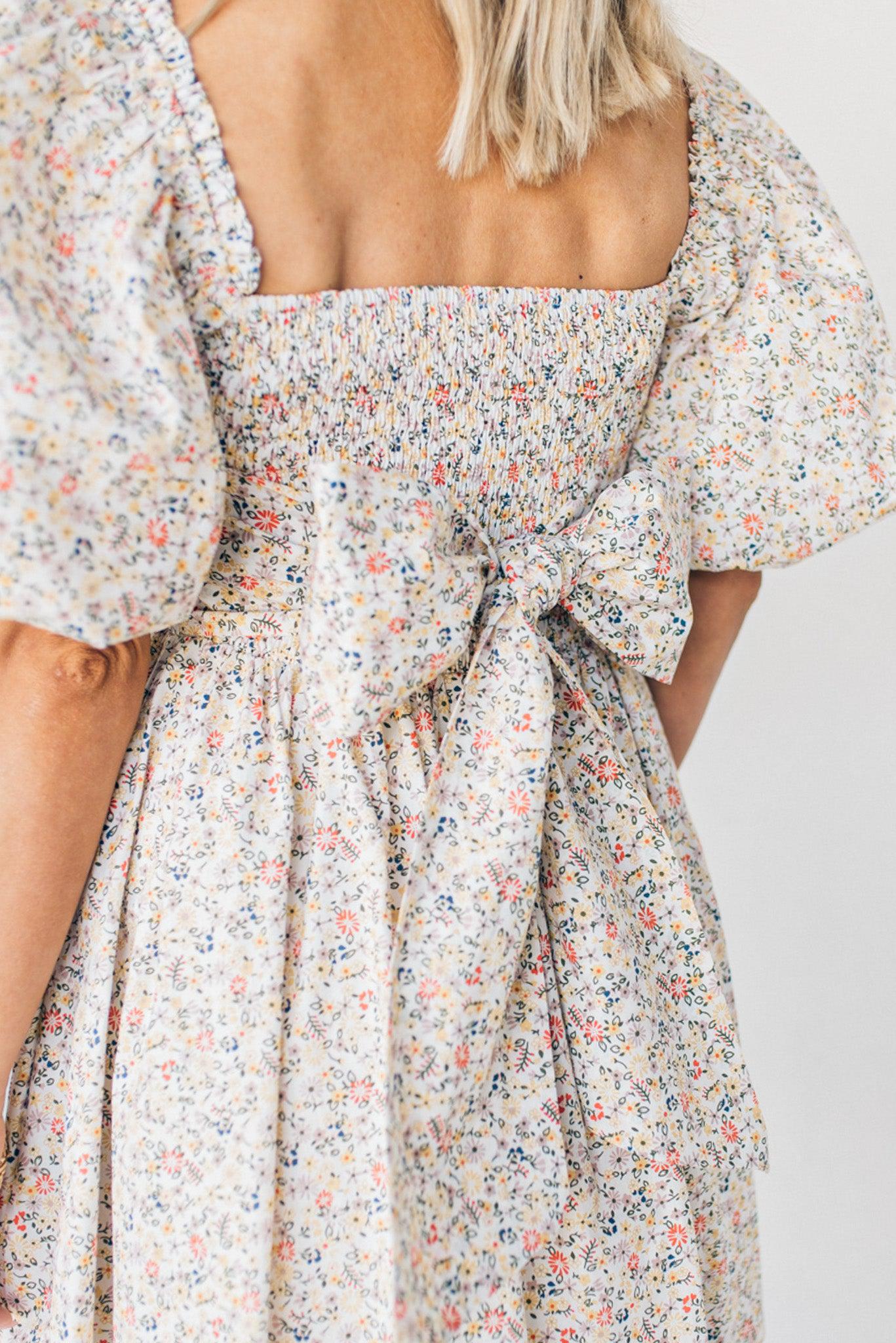 Blonde woman wearing a floral dress with puff sleeves and a large statement bow at the back.