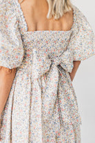 Blonde woman wearing a floral dress with puff sleeves and a large statement bow at the back.
