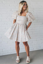 Blonde woman wearing a floral dress with puff sleeves and a large statement bow at the back.