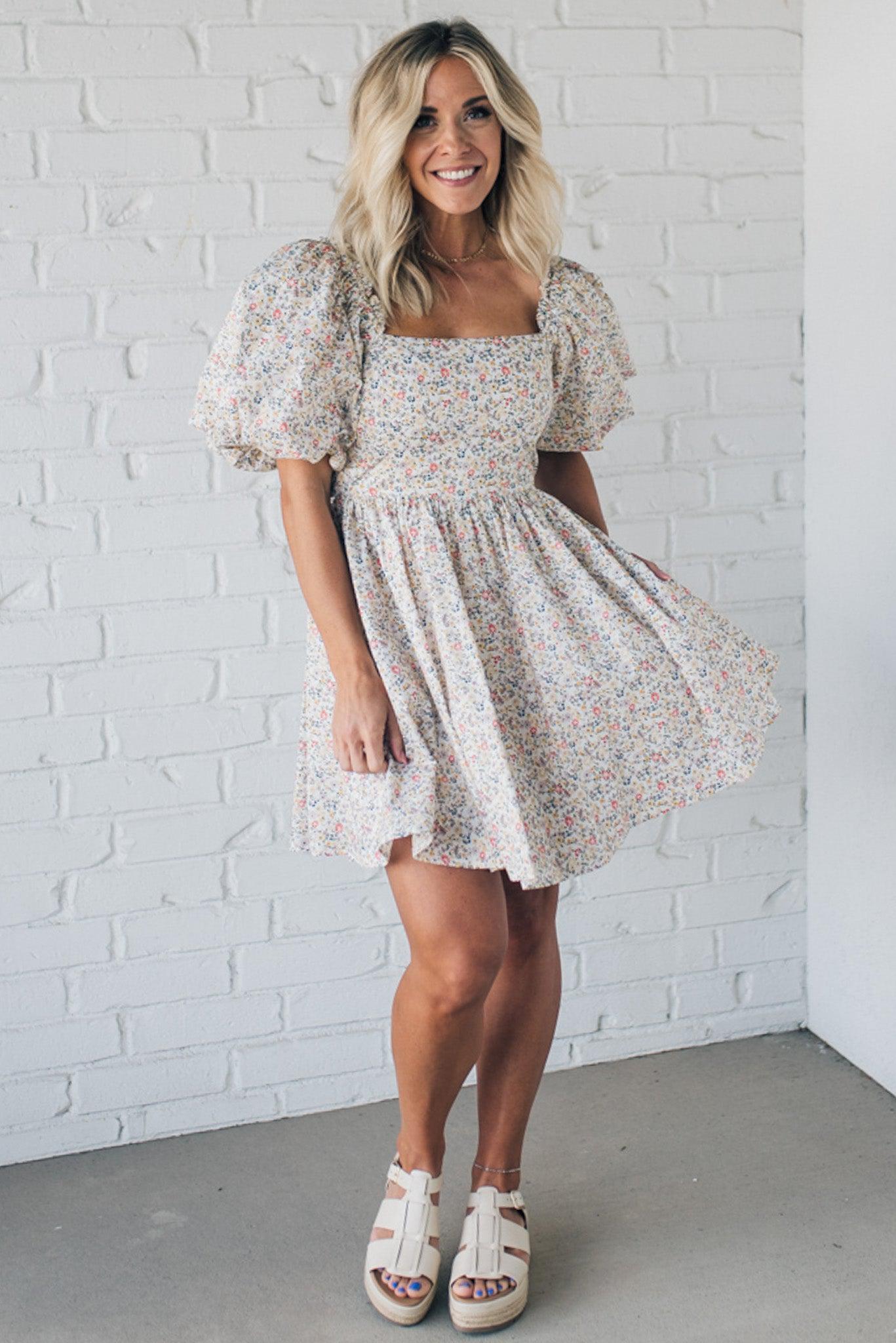 Blonde woman wearing a floral dress with puff sleeves and a large statement bow at the back.