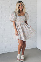 Blonde woman wearing a floral dress with puff sleeves and a large statement bow at the back.