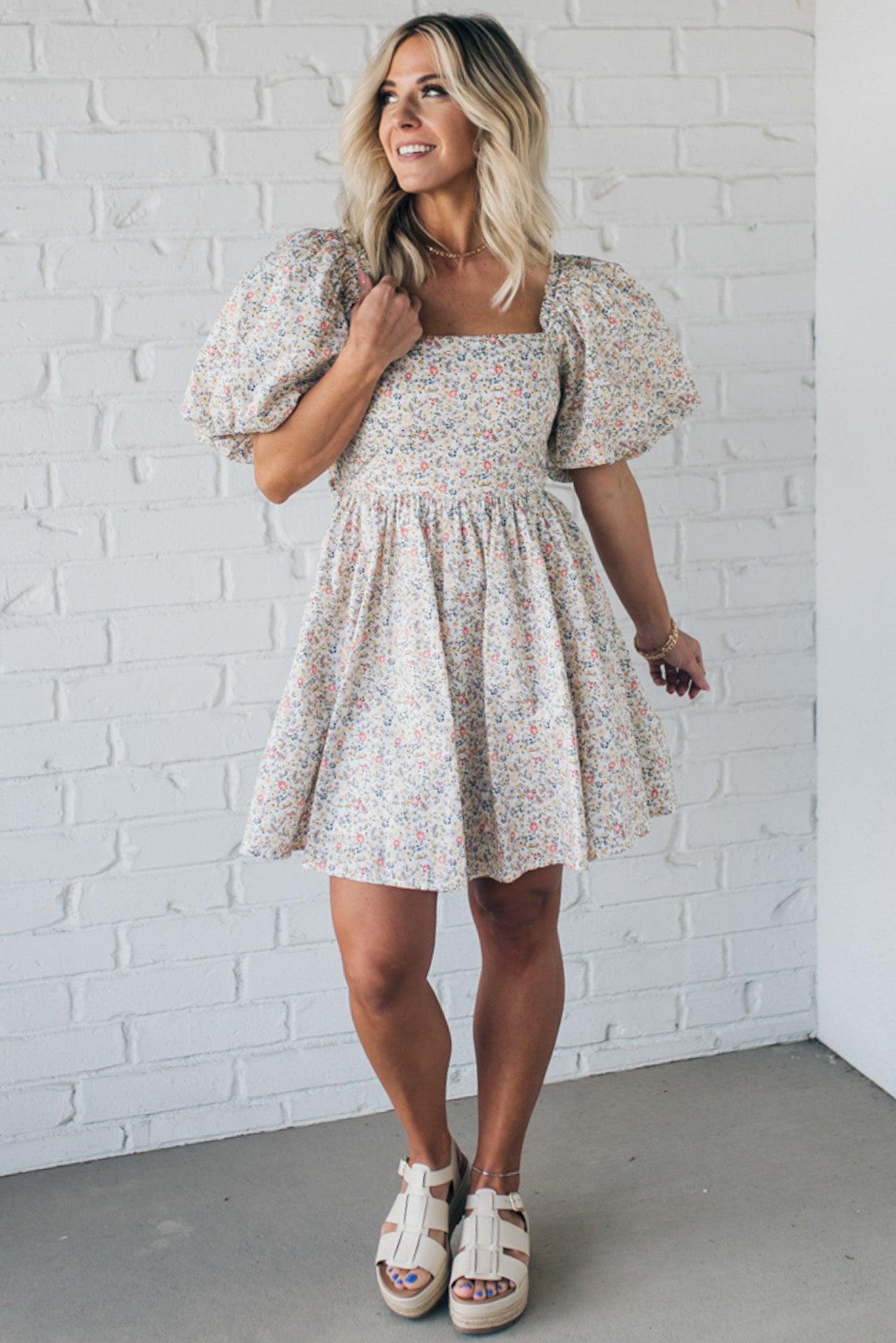 Blonde woman wearing a floral dress with puff sleeves and a large statement bow at the back.