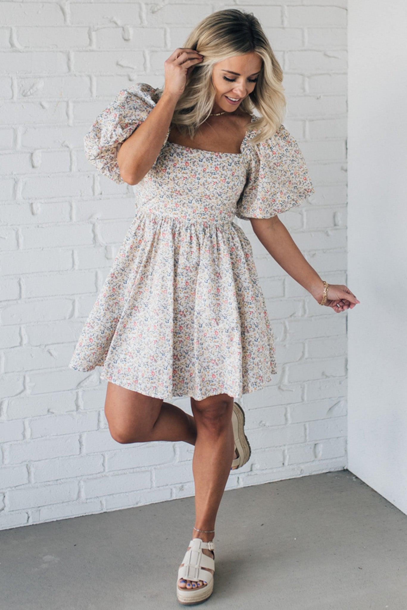 Blonde woman wearing a floral dress with puff sleeves and a large statement bow at the back.