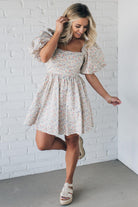 Blonde woman wearing a floral dress with puff sleeves and a large statement bow at the back.