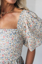 Blonde woman wearing a floral dress with puff sleeves and a large statement bow at the back.