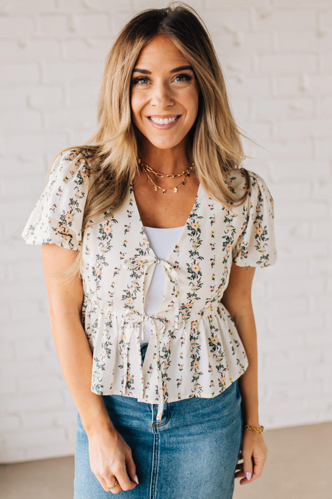 Blonde woman wearing a floral print tie front shirred hem blouse top with puff sleeve.