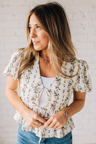 Blonde woman wearing a floral print tie front shirred hem blouse top with puff sleeve.