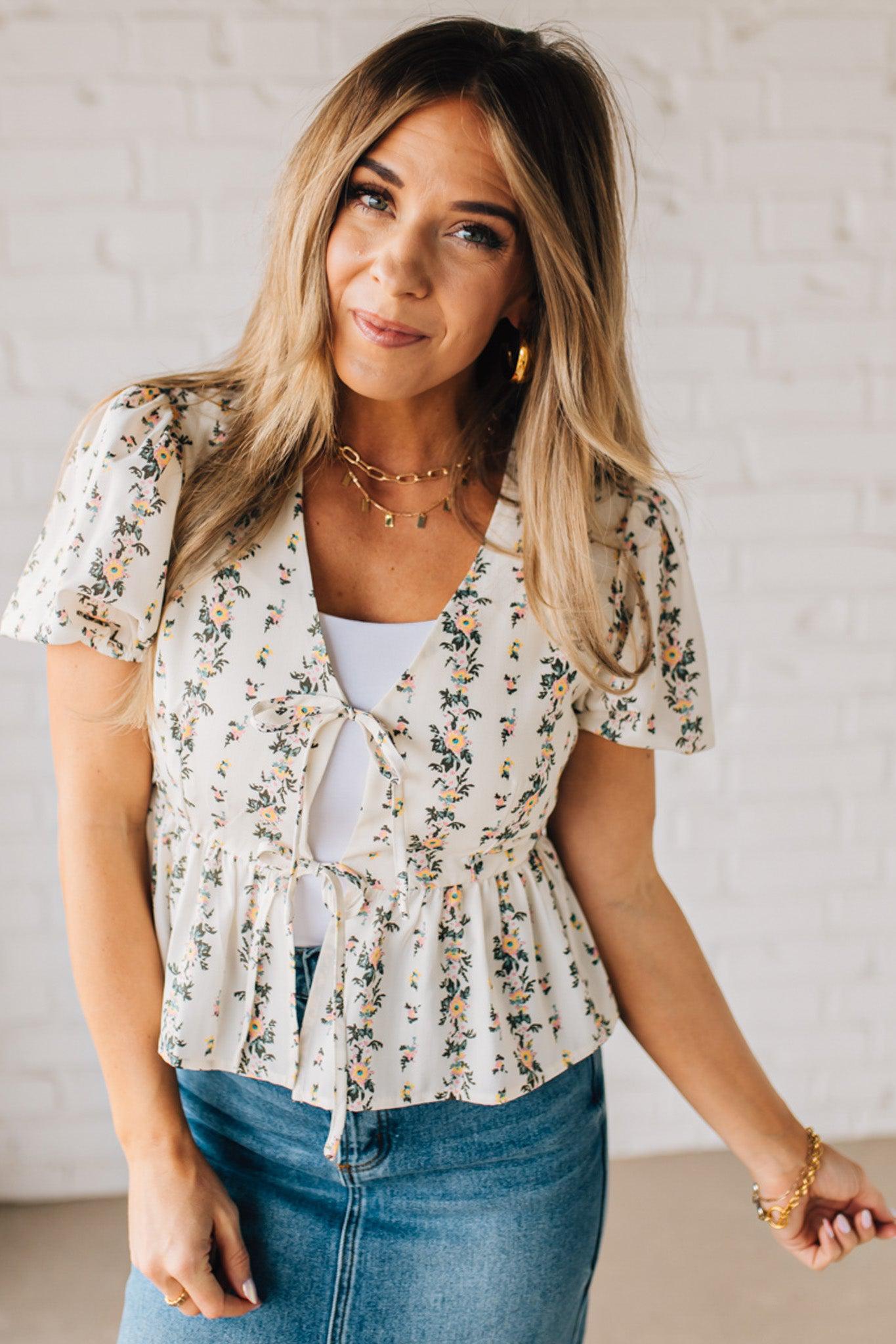 Blonde woman wearing a floral print tie front shirred hem blouse top with puff sleeve.