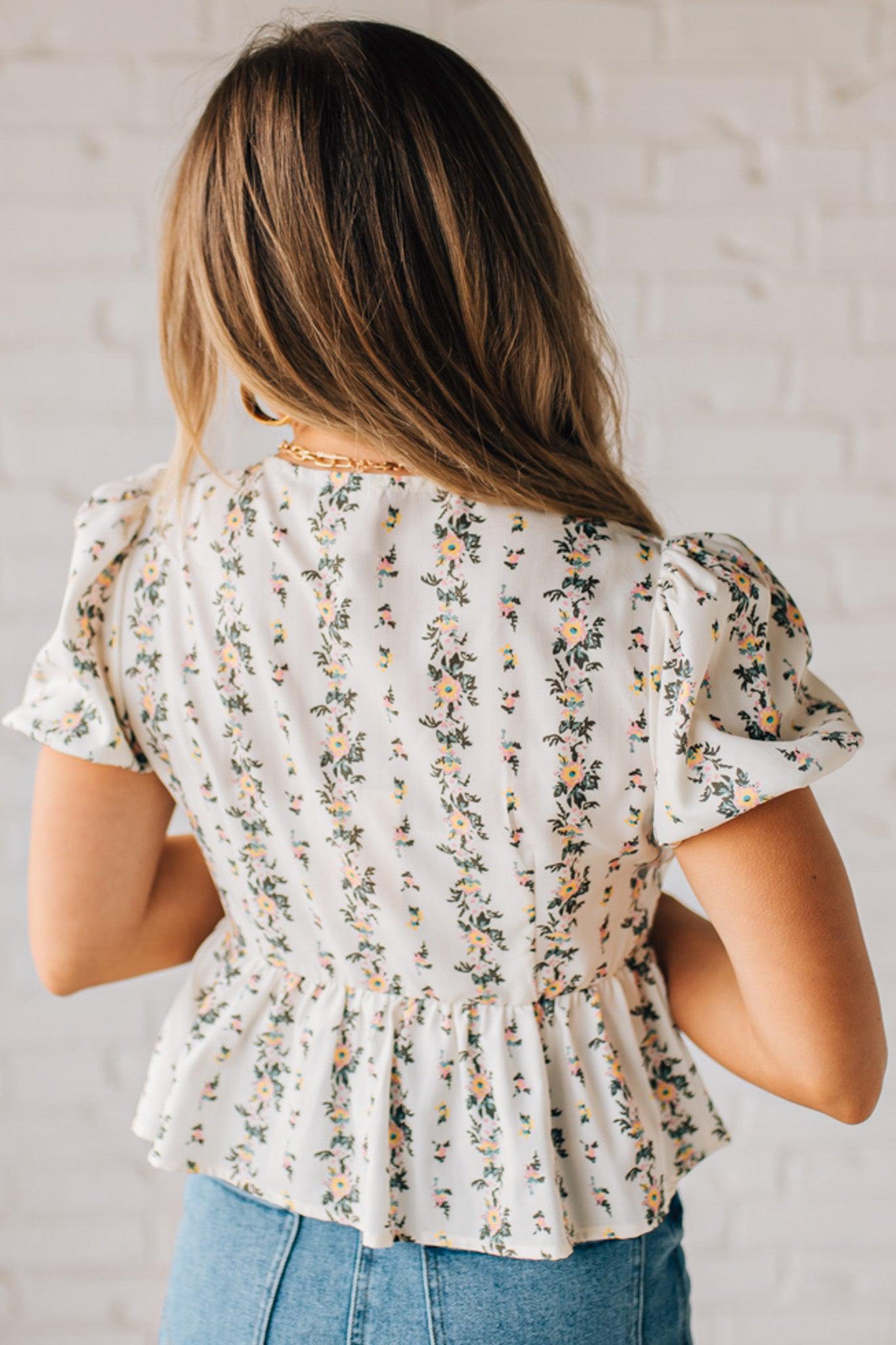 Blonde woman wearing a floral print tie front shirred hem blouse top with puff sleeve.